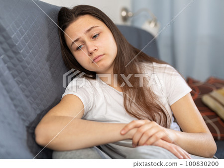 Upset girl sitting on sofa at home 100830200
