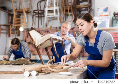 Skilled female furniture repair specialist in uniform restoring Victorian chair during workday in workshop Skilled female furniture repair specialist in uniform restoring Victorian chair during workday in workshop 100830282