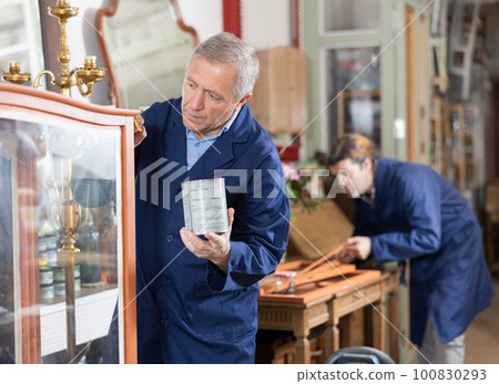 Process of restoring vintage chest of drawers - an craftsman applies protective varnish with brush Process of restoring vintage chest of drawers - an craftsman applies protective varnish with brush 100830293
