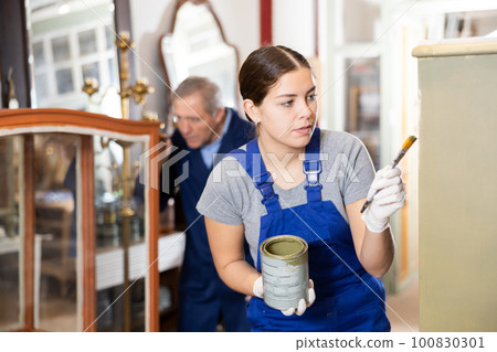Female furniture maker applies protective varnish with brush to wooden parts of vintage cabinet Female furniture maker applies protective varnish with brush to wooden parts of vintage cabinet 100830301