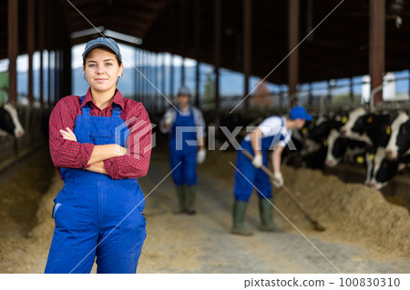 Portrait of positive female farm worker in cowshed Portrait of positive female farm worker in cowshed 100830310