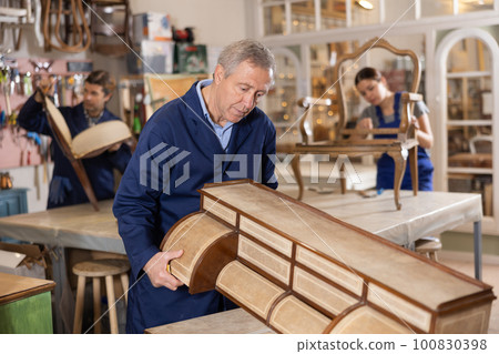 Older male furniture maker sanding vintage commode in workshop 100830398
