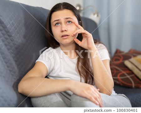 Upset girl sitting on sofa at home 100830401