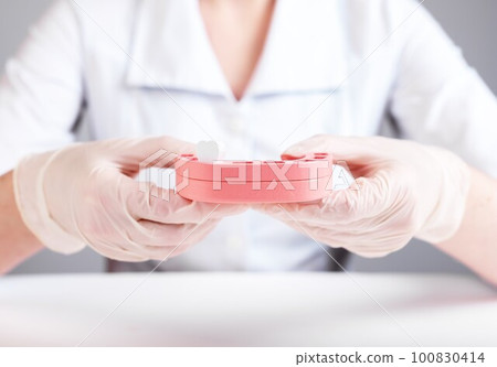 Dentist holding jaw model with single tooth. Implantation or teeth loss caused by no professional dental care, poor oral hygiene, gums diseases, traumas. Doctor in lab coat and in gloves. photo 100830414