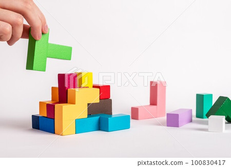 Hand assembling tetris puzzle, searching appropriate place for wooden block. Construction, formation concept. Finding solution to problem. Logical thinking, reasoning strategy development. photo Hand assembling tetris puzzle, searching appropriate place for wooden block. Construction, formation concept. Finding solution to problem. Logical thinking, reasoning strategy development. photo 100830417