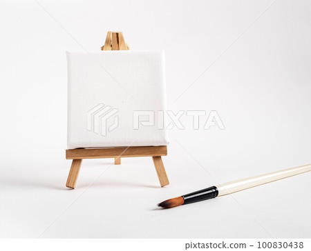 Square canvas on tiny mini easel, blank mockup on wood tripod, paintbrush. Artistic supplies composition. High quality photo Square canvas on tiny mini easel, blank mockup on wood tripod, paintbrush. Artistic supplies composition. High quality photo 100830438