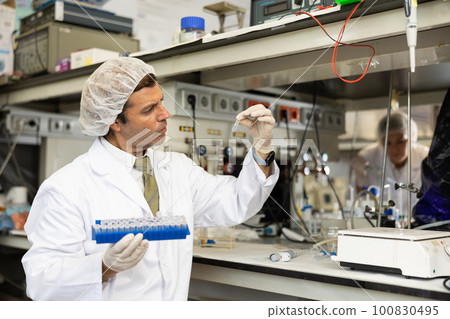 Middle-aged Latin male scientist researcher holding tripod and looking at reaction in test tube while performing biochemical tests in lab Middle-aged Latin male scientist researcher holding tripod and looking at reaction in test tube while performing biochemical tests in lab 100830495