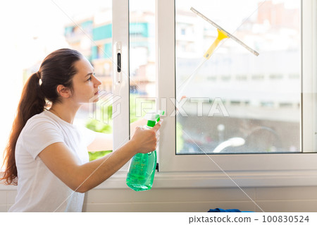 Young positive woman doing chores cleaning window Young positive woman doing chores cleaning window 100830524