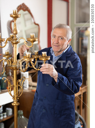 Senior restorer with brush removes dirt and dust deposits from bedside antique floor lamp 100830530