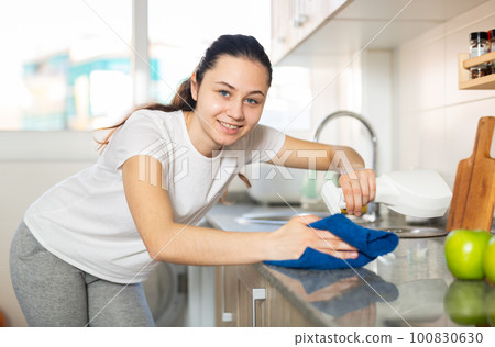 Young positive woman doing chores cleaning kitchen Young positive woman doing chores cleaning kitchen 100830630