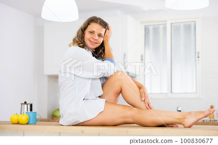 Portrait of attractive woman sitting on kitchen table 100830677