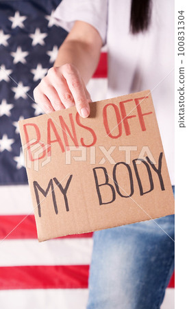 Woman holding a sign Bans Off My Body American flag on background. Protest against anti abortion law. Women's strike. Womens rights freedom. 100831304
