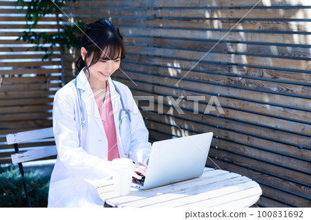 A female doctor in a white coat using a laptop on the terrace 100831692