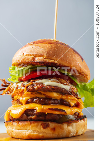 Loaded cheeseburgers three triple, stacked patties stacked high with layers of cheese, lettuce, and tomato. Tall cheeseburger. High quality photo Loaded cheeseburgers three triple, stacked patties stacked high with layers of cheese, lettuce, and tomato. Tall cheeseburger. High quality photo 100837524