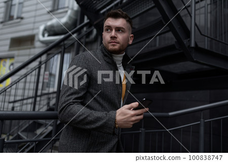 brutal freelancer man with a phone in his hands on the background of a city building brutal freelancer man with a phone in his hands on the background of a city building 100838747