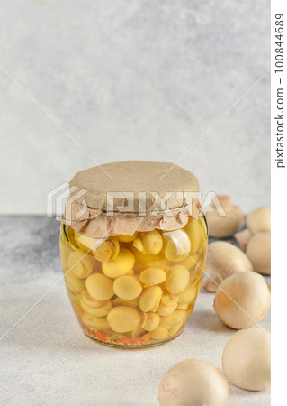 Glass jar with pickled mushrooms champignons on a light background. Chapminions on white background with copy space. Fresh and marinated mushrooms.  100844689