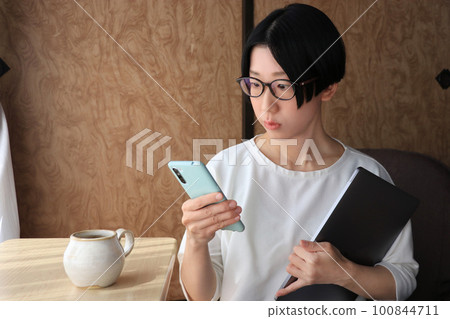 A woman wearing glasses with a troubled face looking at her smartphone 100844711