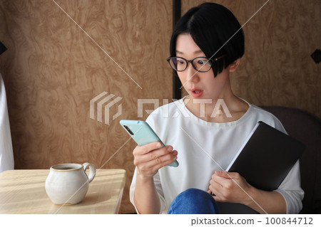 A woman wearing glasses who is surprised to see a smartphone 100844712