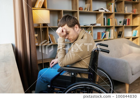 A young handsome man in a wheelchair looks out the window with a sad look 100844830
