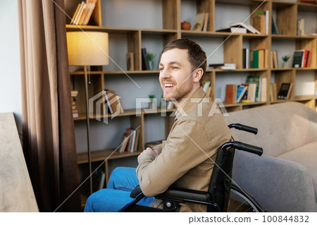 Man on wheelchair in room looking through window and smiling. Side view of young disabled patient in wheelchair looking out window Man on wheelchair in room looking through window and smiling. Side view of young disabled patient in wheelchair looking out window 100844832
