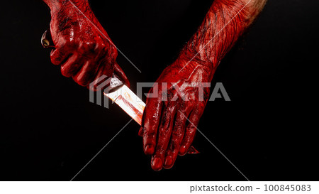 A man wipes a bloody knife with his hand on a black background.  A man wipes a bloody knife with his hand on a black background.  100845083