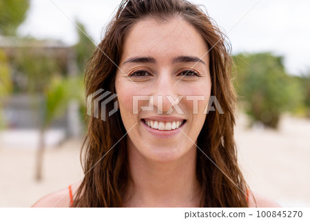 Portrait of happy biracial woman looking at camera and smiling at beach 100845270