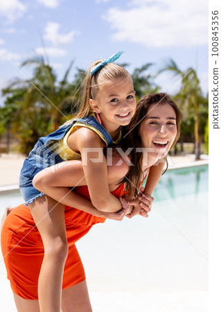 Portrait of happy biracial mother and daughter embracing by the swimming pool Portrait of happy biracial mother and daughter embracing by the swimming pool 100845356