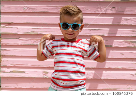 Portrait of happy biracial boy smiling and showing muscles over pink wall Portrait of happy biracial boy smiling and showing muscles over pink wall 100845376