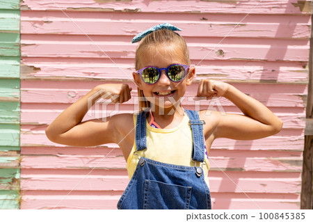 Portrait of happy biracial girl smiling and showing muscles over pink wall 100845385
