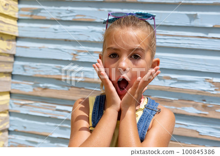 Portrait of surprised biracial girl holding her face with mouth open over blue wall Portrait of surprised biracial girl holding her face with mouth open over blue wall 100845386