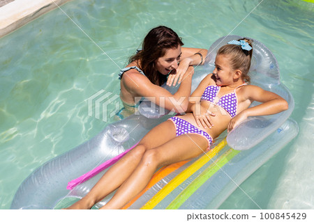 Happy biracial mother and daughter playing together in swimming pool 100845429