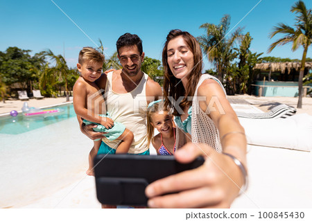Happy biracial family taking selfie by the swimming pool 100845430