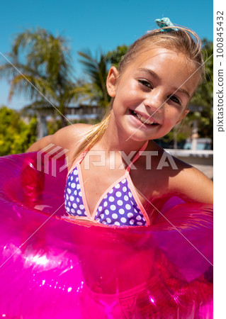 Portrait of happy biracial girl smiling and holding swim ring by the swimming pool Portrait of happy biracial girl smiling and holding swim ring by the swimming pool 100845432