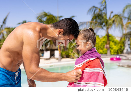 Happy biracial father and daughter using towel by the swimming pool 100845446