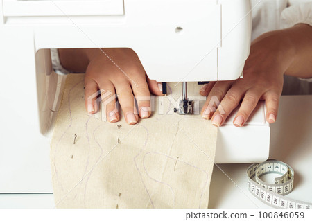 Close up dressmaker hands use sewing machine, place soft fabric with stitch contour on needle plate under presser foot 100846059
