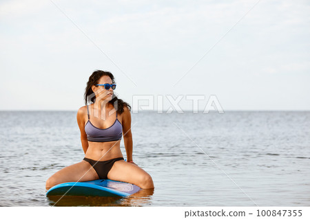 Surfer girl waiting for a wave in the water at sunset Surfer girl waiting for a wave in the water at sunset 100847355