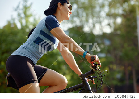 A woman aged 35-45 rides a bike in handicap glasses outside the city, training on a bike, cardio load during cycling 100847425