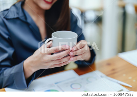 Portrait of a happy Asian woman smiling at her desk during the daytime coffee break. Portrait of a happy Asian woman smiling at her desk during the daytime coffee break. 100847582
