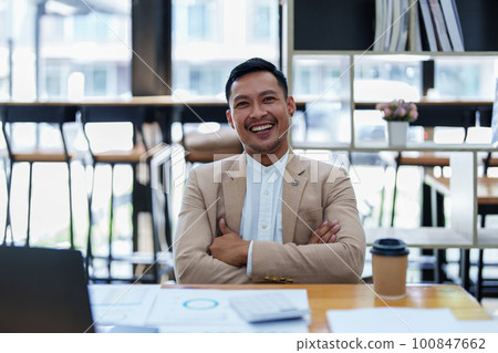Portrait of a male business owner showing a happy smiling face as he has successfully invested his business using computers and financial budget documents at work. 100847662