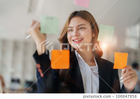 Beautiful young teen asian businesswoman using note pad thinking with planning working on financial document, tax, exchange, accounting and Financial advisor. 100847858