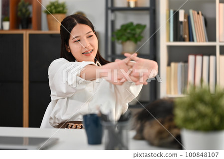 Pleasant asian female worker taking a break, stretching arms at her working desk in home office Pleasant asian female worker taking a break, stretching arms at her working desk in home office 100848107