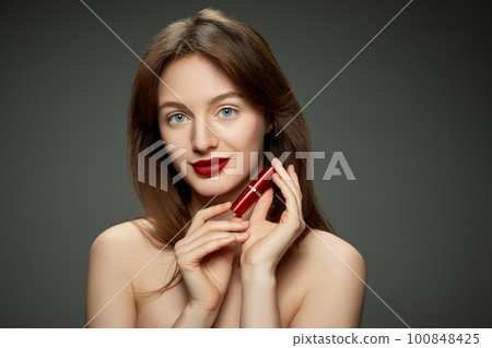 Makeup products. Beautiful young brunette girl with red lips against grey studio background 100848425