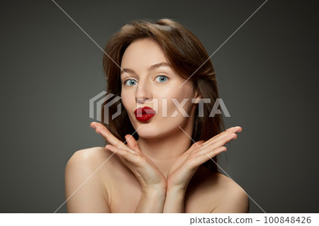 Portrait of young attractive girl with bright red lips makeup against grey studio background Portrait of young attractive girl with bright red lips makeup against grey studio background 100848426
