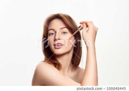 Beautiful with healthy, spotless, clear skin applying face serum, taking care after skin condition against white background Beautiful with healthy, spotless, clear skin applying face serum, taking care after skin condition against white background 100848445