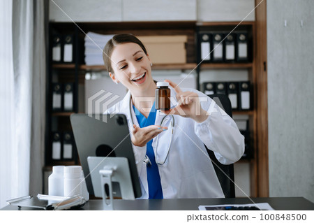 Attractive female doctor talking while explaining medical treatment to patient through a video call with laptop in office. 100848500