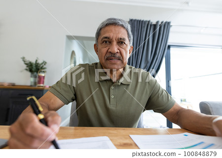 Portrait of serious biracial senior man analyzing bills on wooden table while sitting at home 100848879