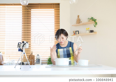 A woman recording a cooking video in front of the camera 100848941