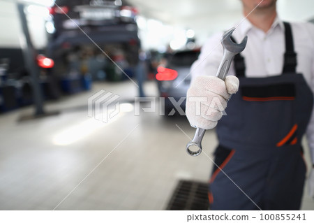 Car repairman in uniform holds wrench in car workshop Car repairman in uniform holds wrench in car workshop 100855241