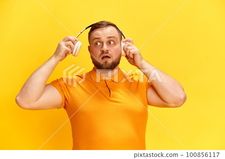 One confused man hears strange noise with surprised facial expression over yellow background One confused man hears strange noise with surprised facial expression over yellow background 100856117