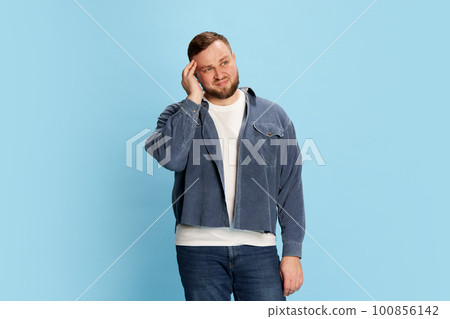 Portrait of bearded confused man standing and thinking with unconfident facial expression over blue background 100856142